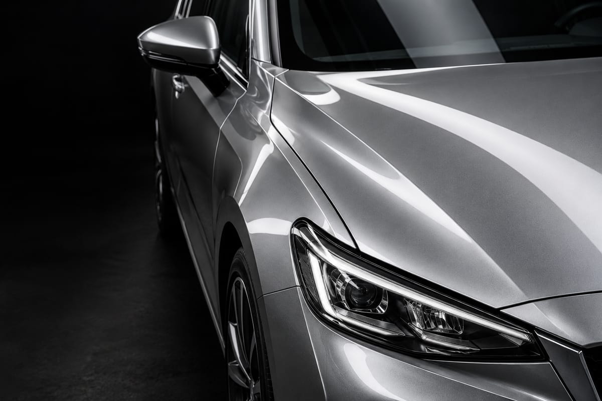 Illustrative silver car paint and headlight in a dark studio