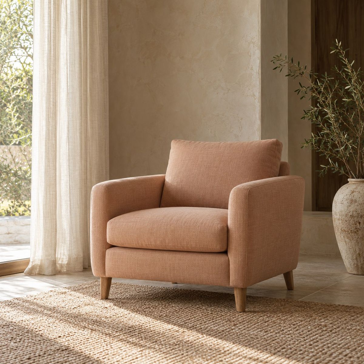 An empty peach armchair beside a linen curtain in a quiet sunlit room